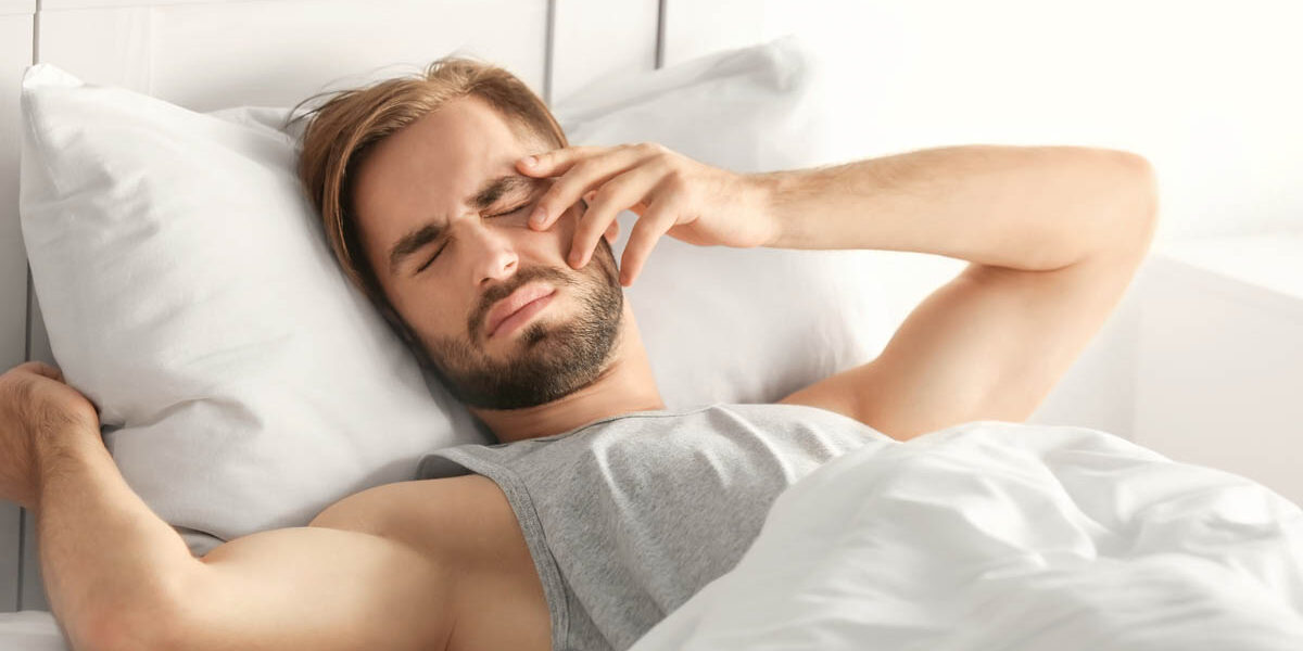 Morning of young man suffering from hangover at home man struggling to get up and out of bed believes he is suffering with the signs of alcoholism