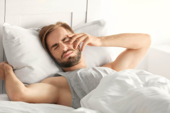 Morning of young man suffering from hangover at home man struggling to get up and out of bed believes he is suffering with the signs of alcoholism