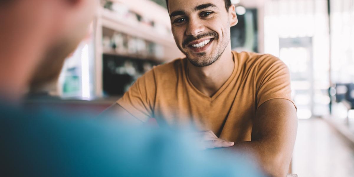 What to Know When Dating a Recovering Alcoholic a man smiles while sitting with another man and thinks about how he is dating a recovering alcoholic