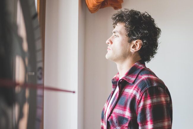 man stands and stares out his window thinking about synthetic drug addiction