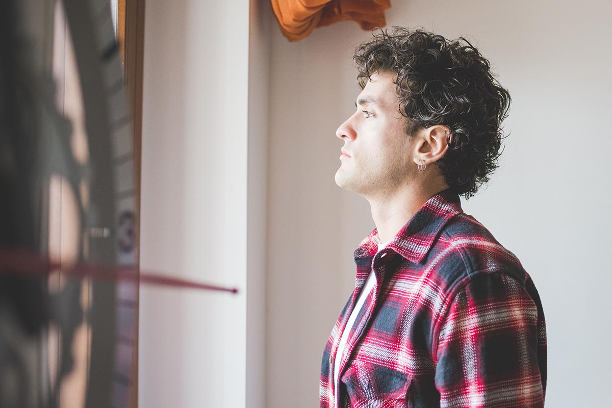 What Are the Signs of Synthetic Drug Addiction man stands and stares out his window thinking about synthetic drug addiction