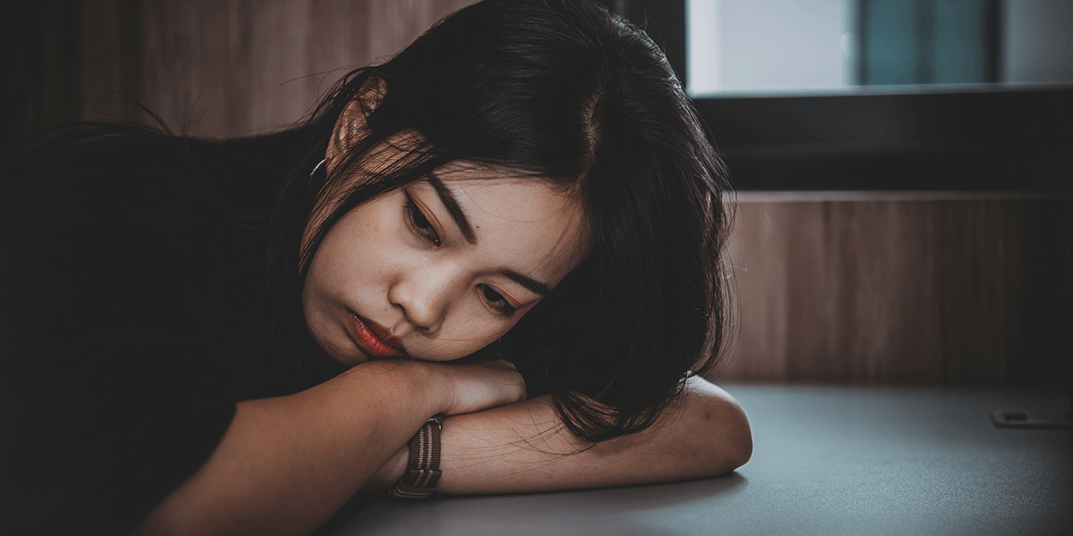 a young woman rests her head on her arms on a table in the dark struggling with the realization she might need opioid treatment