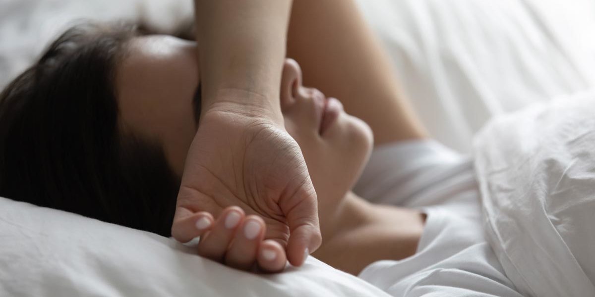 woman lies in bed with her forearm covering her eyes while struggling with heroin withdrawal symptoms