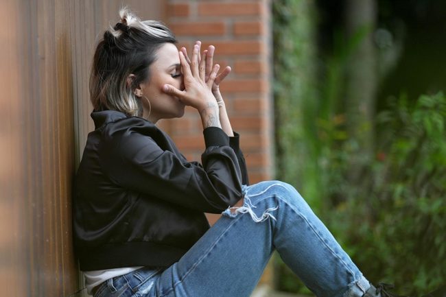 a woman sits and leans against a wall outside while struggling with some cocaine addiction symptoms