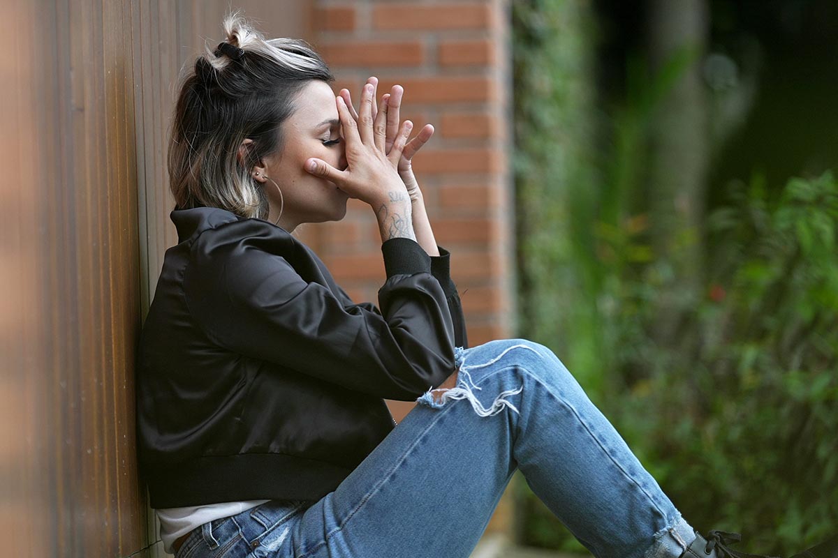 a woman sits and leans against a wall outside while struggling with some cocaine addiction symptoms
