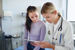 a doctor sits with a young adult patient while looking at a tablet and explaining to her about her co-occurring disorder