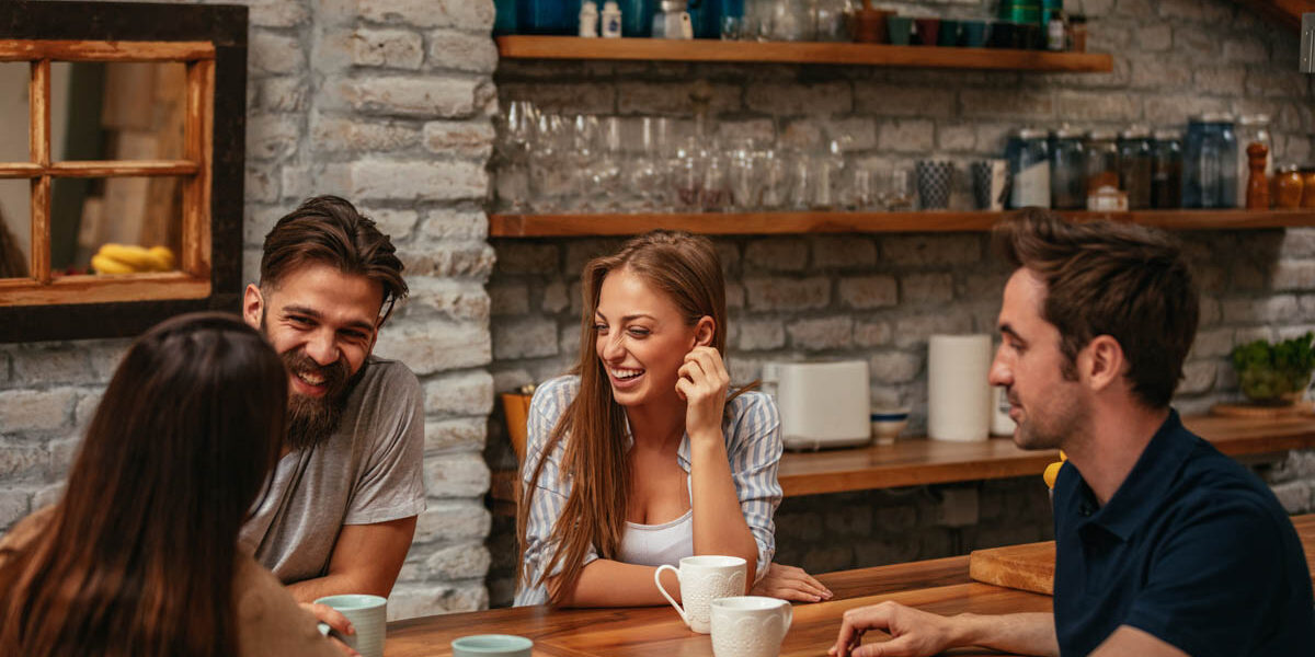 5 Benefits of Non-Alcoholic Drinks a group of friends sit in a kitchen area enjoying non-alcoholic drinks and socializing