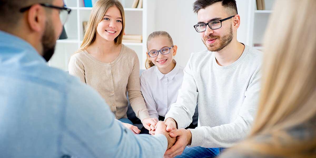 3-Goals-Of-Family-Therapy-For-Communication a family sits together in a circle reaching out to each others hands and discussing their goals for family therapy