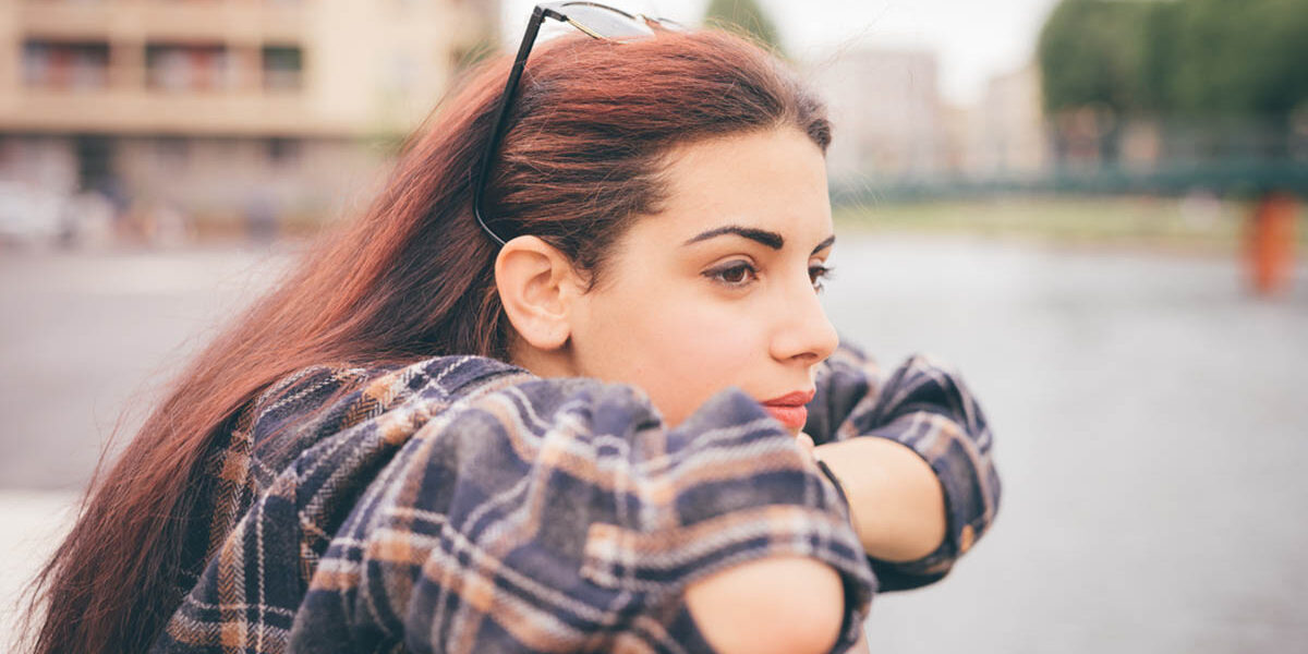 Young beautiful reddish brown hair girl a woman leans on a ledge while outside and looks afar thinking about if she is showing signs of being a functional alcoholic