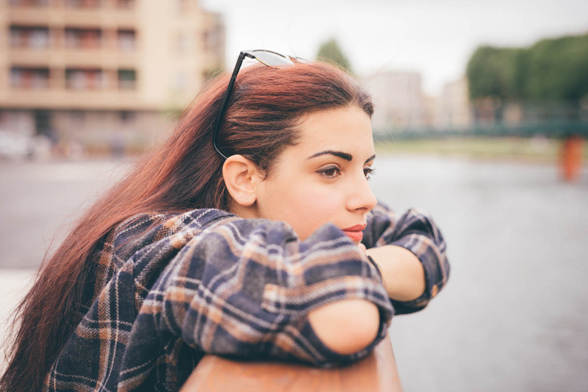 a woman leans on a ledge while outside and looks afar thinking about if she is showing signs of being a functional alcoholic
