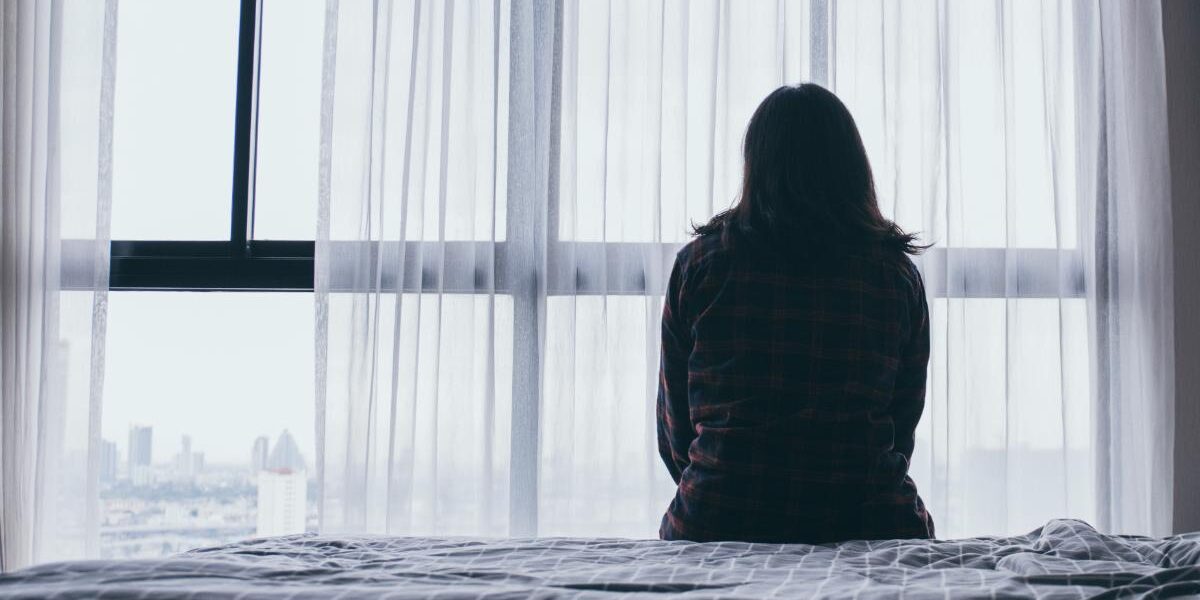 a person sits on their bed and looks out a window while wondering if they are experiencing xanax overdose symptoms