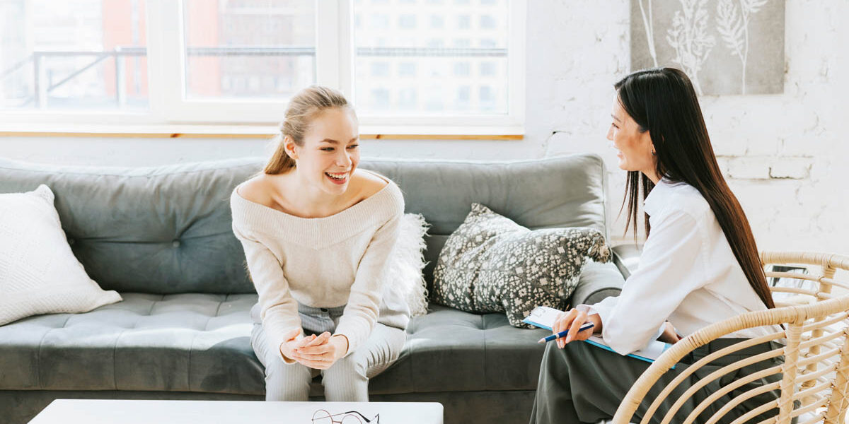 What Is an Addiction Specialist a woman sits on a couch and leans over while talking to a addiction specialist who is siting in a chair listening to the woman