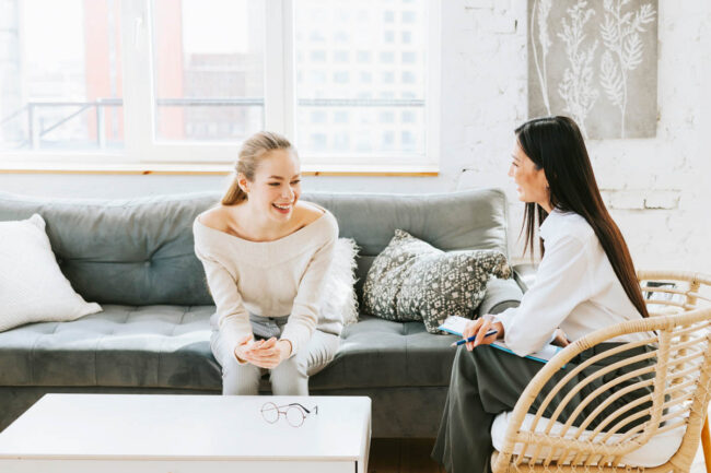 What Is an Addiction Specialist a woman sits on a couch and leans over while talking to a addiction specialist who is siting in a chair listening to the woman