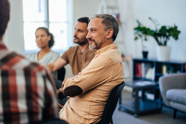 Therapy for Rehabilitation for Alcoholism a group of people sit in group therapy as rehabilitation for alcoholism and listen to each other talk