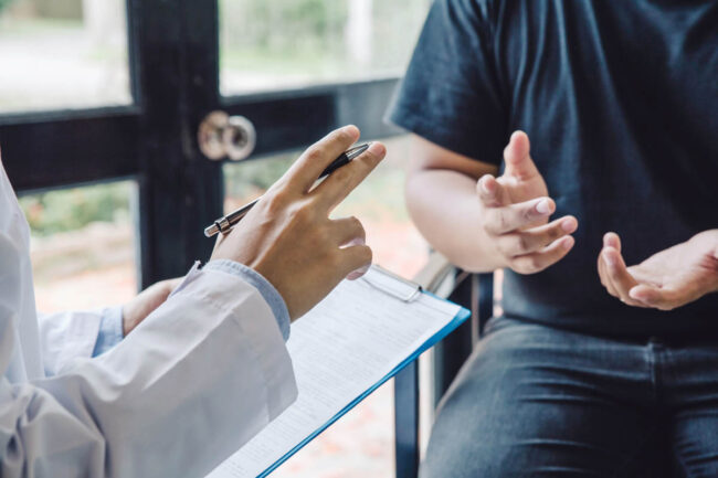 patient moves their hands while asking a specialist about what does php stand for in rehab as the specialist holds a clipboard