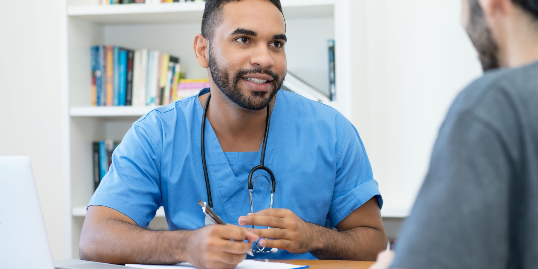 a man in scrubs sits with a patient at a desk at a php facility explaining the type of care to expect in a php