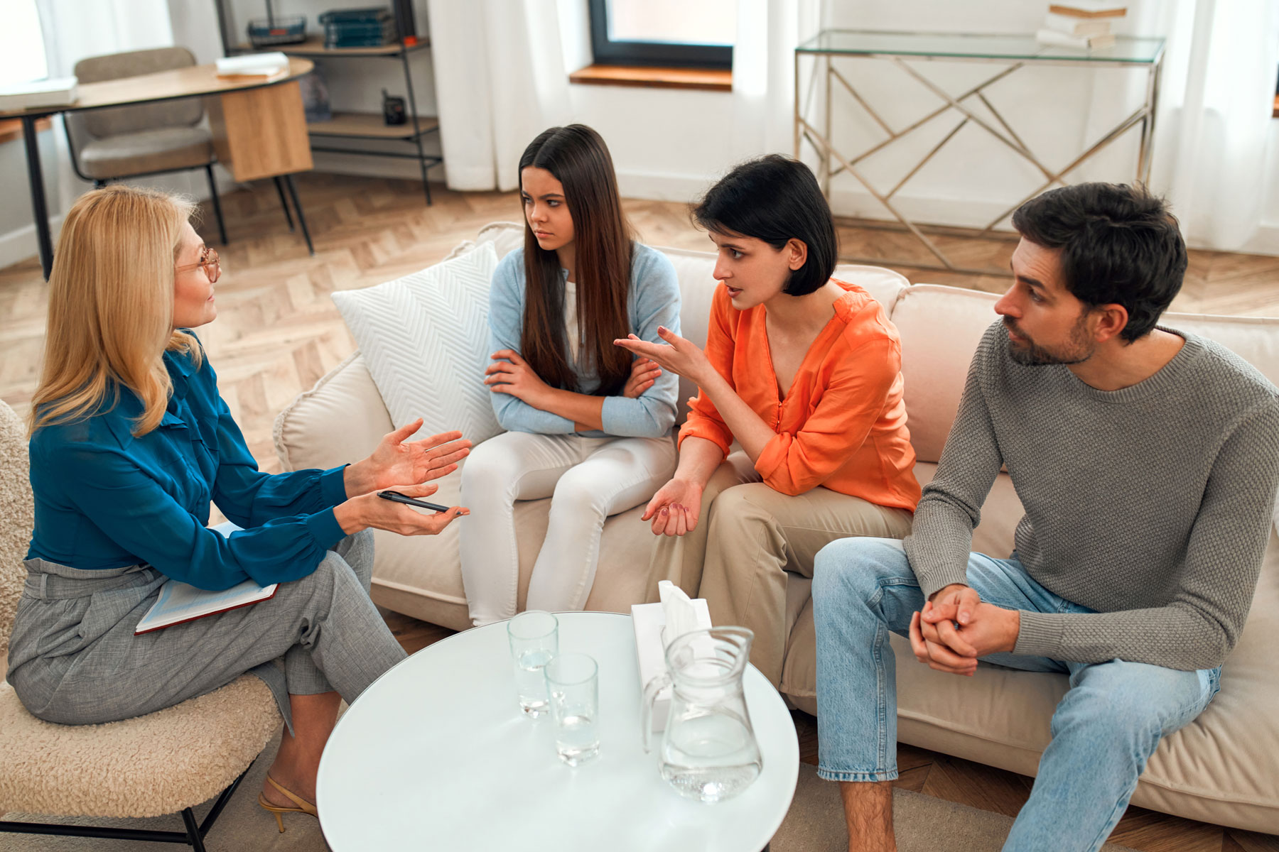 The 5 Stages of Family Therapy – What Are They a family sits together on a couch talking to therapist about stages of therapy