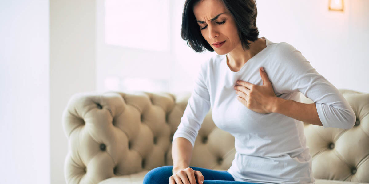 woman sitting on a couch holds her hand to her chest in pain wondering why does my chest hurt after drinking