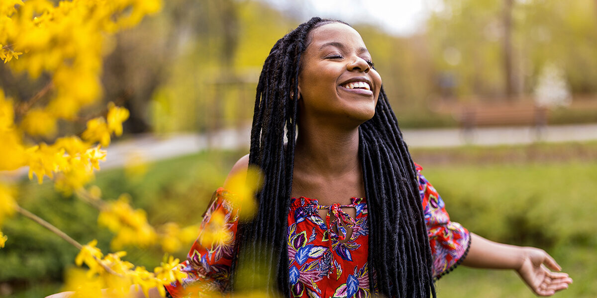The Role of Mindfulness in Recovery a smiling women stands outside with her eyes closed and arms stretched embracing mindfulness in recovery