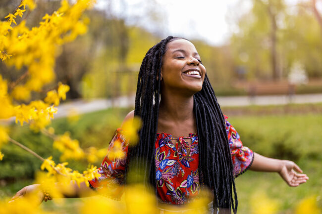 The Role of Mindfulness in Recovery a smiling women stands outside with her eyes closed and arms stretched embracing mindfulness in recovery