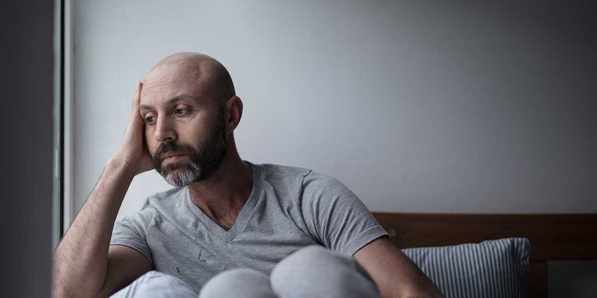 Recognizing-Ketamine-Addiction-Symptoms-Know-the-Signs a sad bald man with a beard holds hand to side of his head experiencing ketamine addiction symptoms