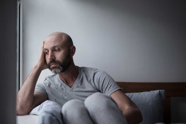 Recognizing-Ketamine-Addiction-Symptoms-Know-the-Signs a sad bald man with a beard holds hand to side of his head experiencing ketamine addiction symptoms