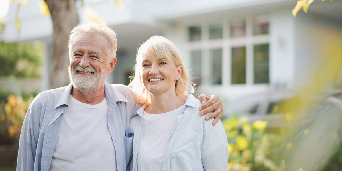 an older adult couple smile while standing outside after learning about the importance of family support in recovery