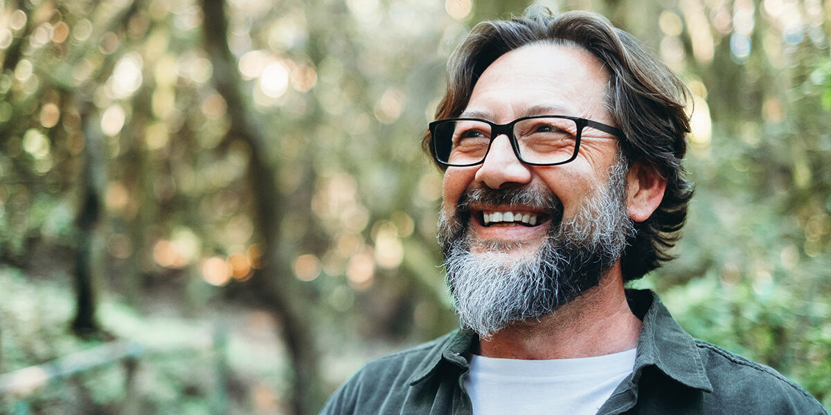 Step-by-Step-Guide-To-Addiction-Recovery older smiling man with glasses stands outside after feeling accomplished from completing his steps to recovery