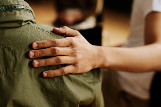 Hand of young supportive man consoling his friend with post traumatic syndrome a person consoles another person showing their role in support groups in recovery by placing their hand on a fellow member's shoulder